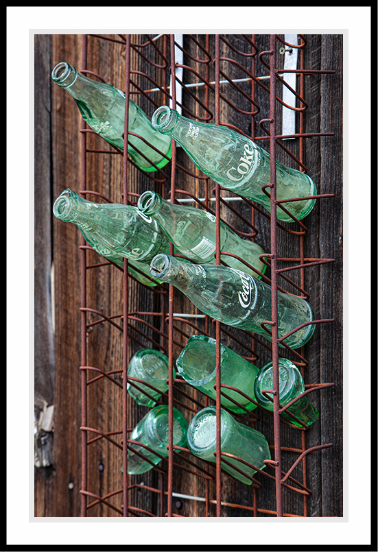 Coke bottles on a shelf hanging on the wall.